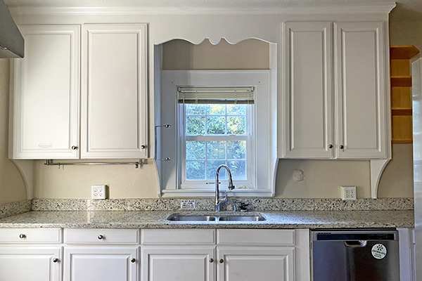 One side of the Recovery Housing kitchen with white cabinets, granite countertop, double sink, and dishwasher